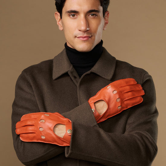 Men's orange lambskin driving gloves with touchscreen, worn with crossed arms