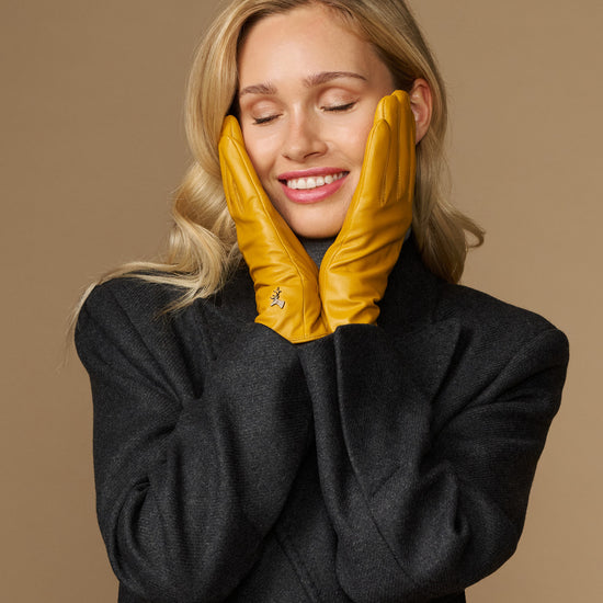 Yellow leather gloves worn on both hands with stitched fingers and snug wrist cuffs