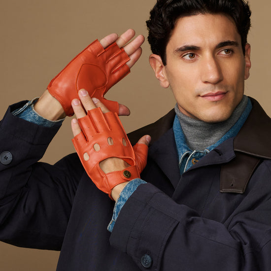 Men's orange fingerless lambskin driving gloves worn with denim cuff and snap tab