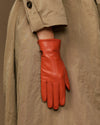 Orange sheepskin leather glove with fleece lining, hanging from a jacket cuff