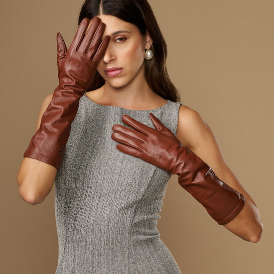 Cognac leather below-elbow gloves with glossy texture, hands positioned near face