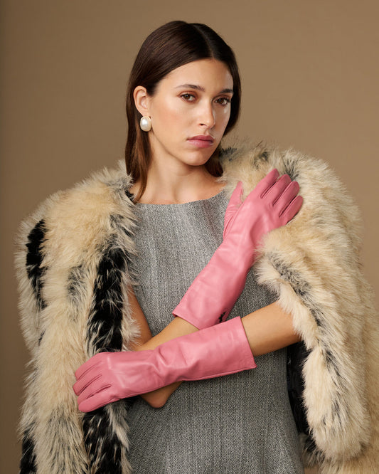 Pink mid-forearm leather gloves worn with a faux-fur jacket; hands posed in front