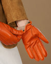 Orange leather glove with buttoned cuff and stitched panels, soft lining visible at wrist