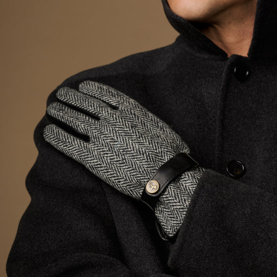 Men's gloves close-up: gray herringbone palm with black leather strap at the wrist.