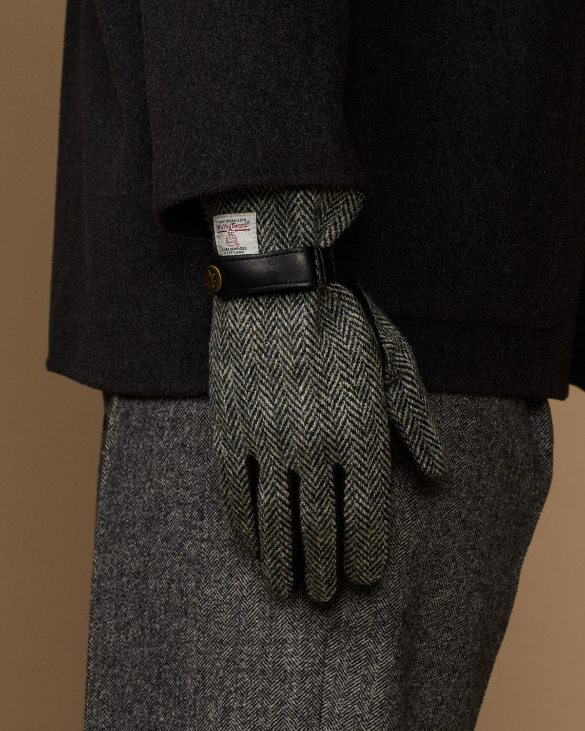 Men's gloves rear view: black leather top and gray herringbone fingers with wrist label.